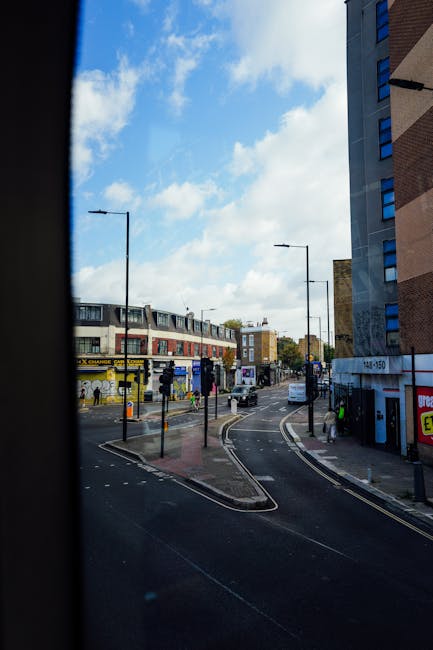 A modern tram operating in the St. James Quarter area, positioned on tracks next to a dark, contemporary building with a reflective surface. The tram has a sleek, white exterior with black-tinted wind